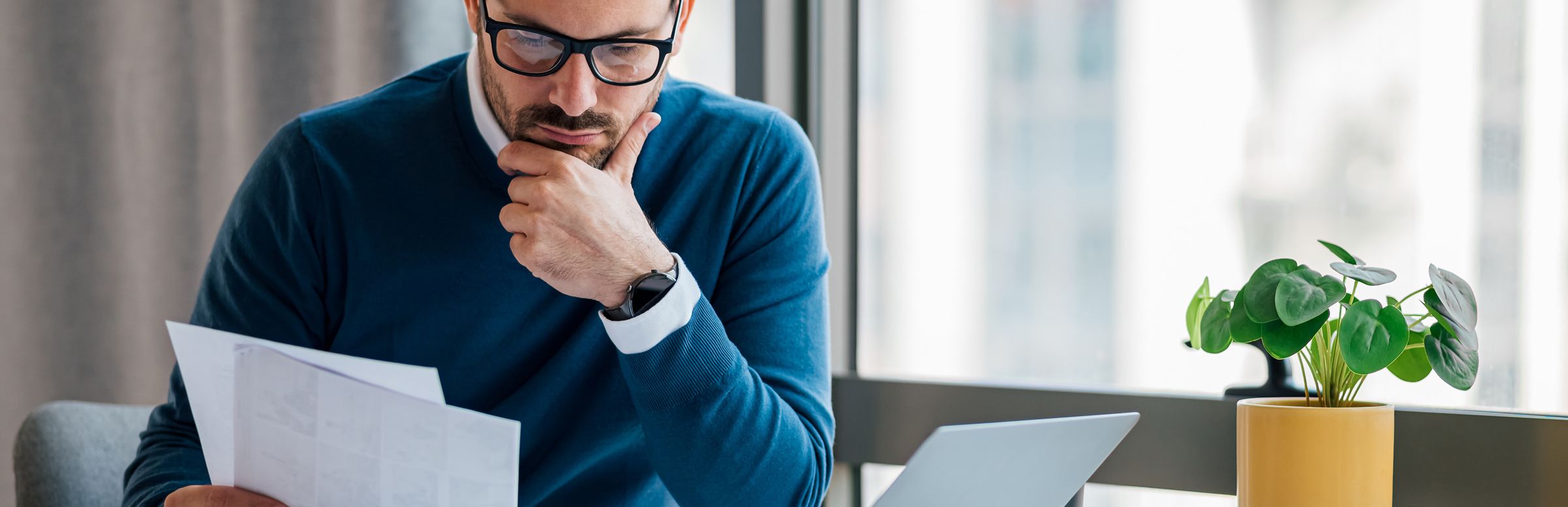 Man reviewing paperwork while sitting with laptop