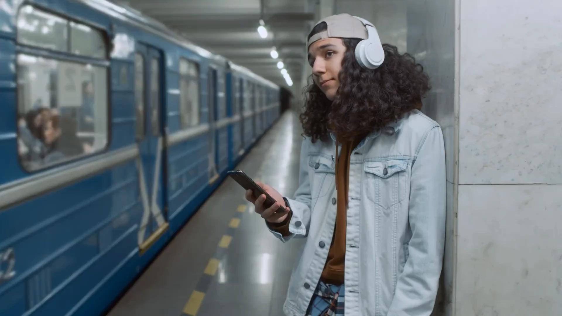 Traveller in headphones checking a phone on a subway platform