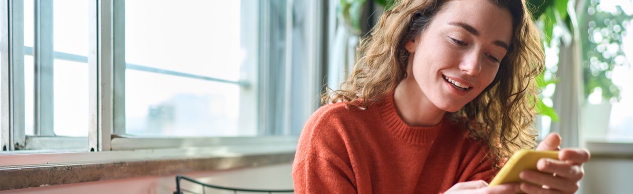 Woman with curly hair smiling at her yellow smartphone