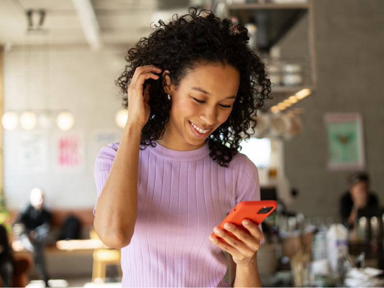 A smiling woman looks at her phone in a warm, sunlit cafe, reacting with genuine relief and satisfaction