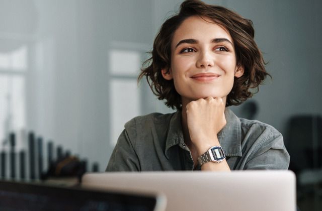 Woman in a gray shirt smiling in front of a laptop
