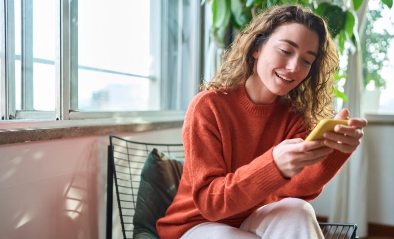 Woman with curly hair smiling at her yellow smartphone