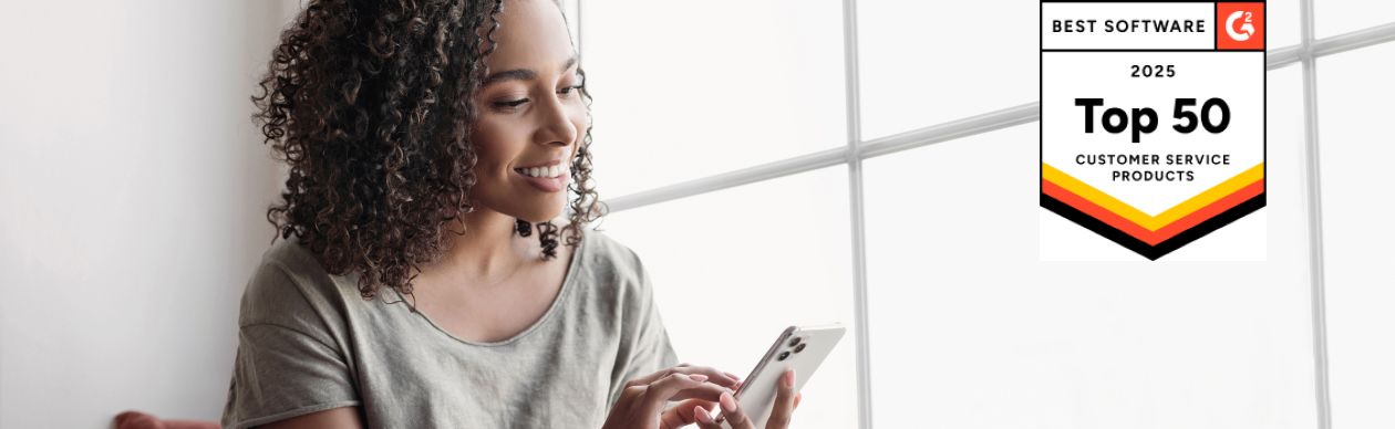 Woman in front of a window smiling down at her phone. On the right is a G2 bade for Top 50 Customer Service Products 2025.
