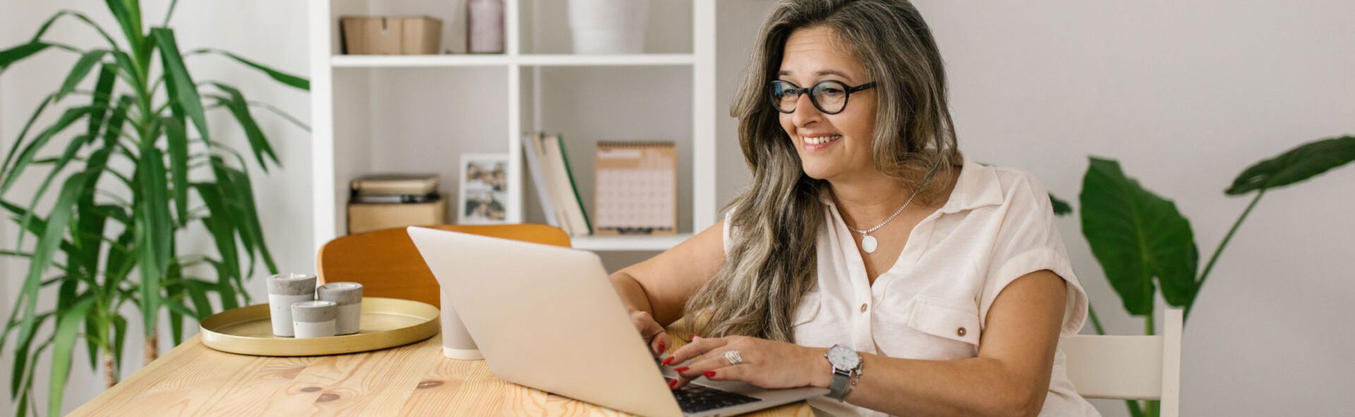 Older woman in glasses typing on a laptop in a dining room