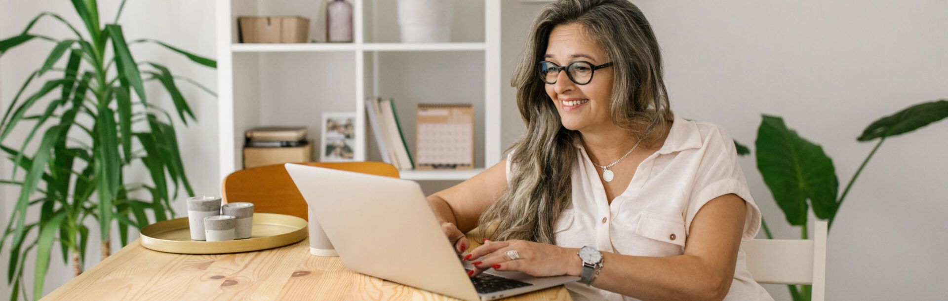 Older woman in glasses typing on a laptop in a dining room