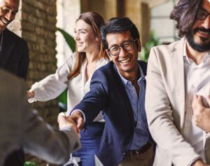 A smiling man reaching out to shake hands with someone among a group of professionals