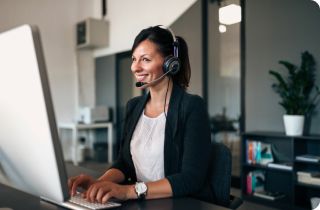 Smiling woman with a headset typing in front of a computer monitor