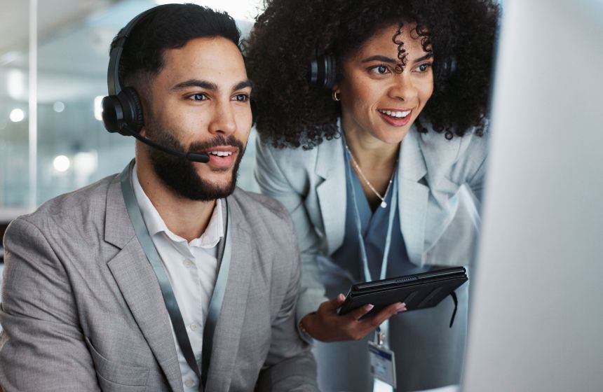 Manager explaining something to customer service agent wearing headset on computer