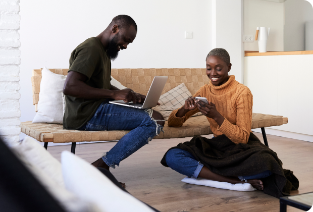 Two people sitting in a living room, a man with a laptop and a woman with a smartphone