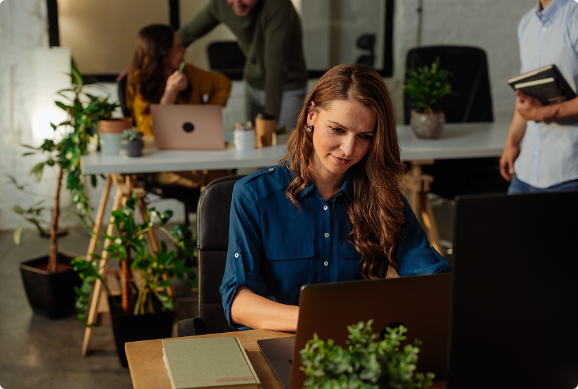 A man with dark hair and a beard, wearing earphones and a green shirt, smiles joyfully while looking at a laptop in a cozy, softly-lit room.