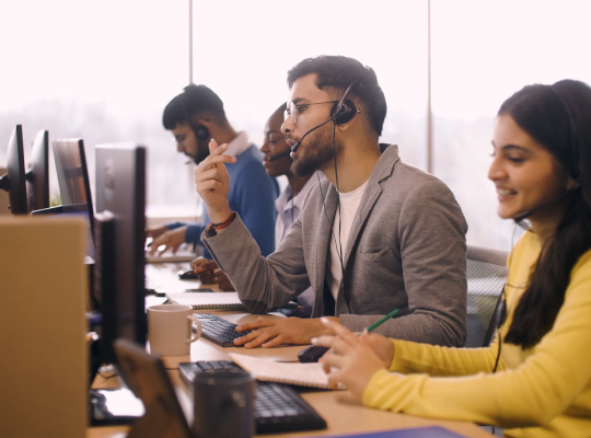 Customer service agents wearing headsets working at computers in an open office.