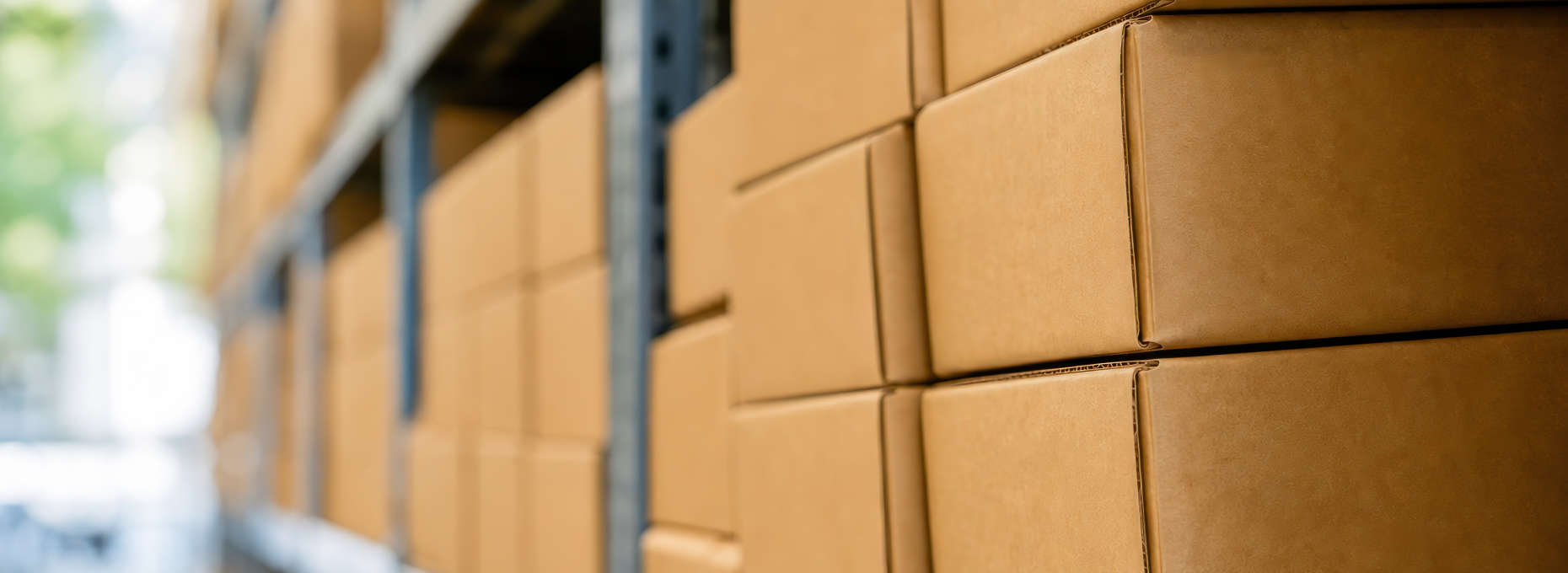 Cardboard shipping boxes stacked on metal warehouse shelving, with the aisle blurred in the background