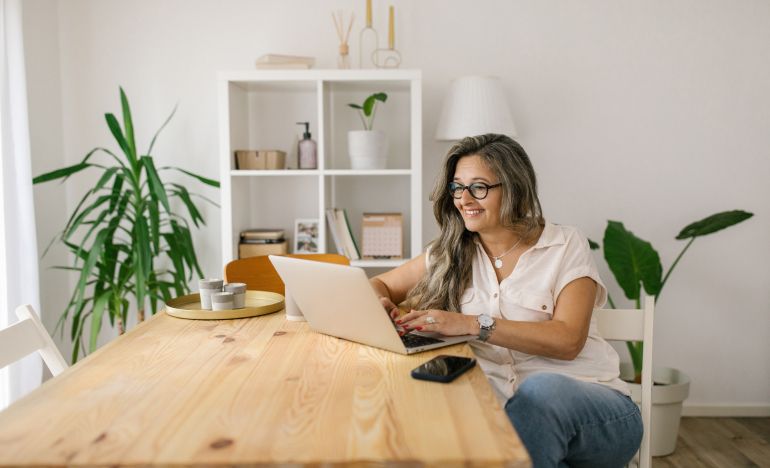 Older woman in glasses typing on a laptop in a dining room