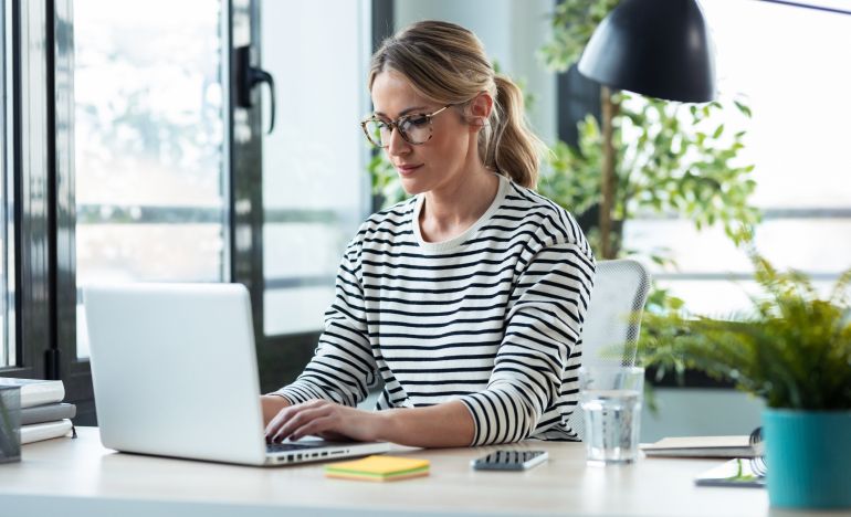 Woman in glasses and a striped shirt working on her laptop