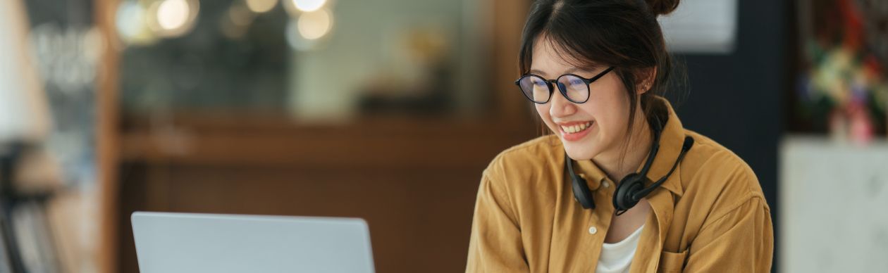 Bespectacled woman in and orange shirt smiling in front of a laptop
