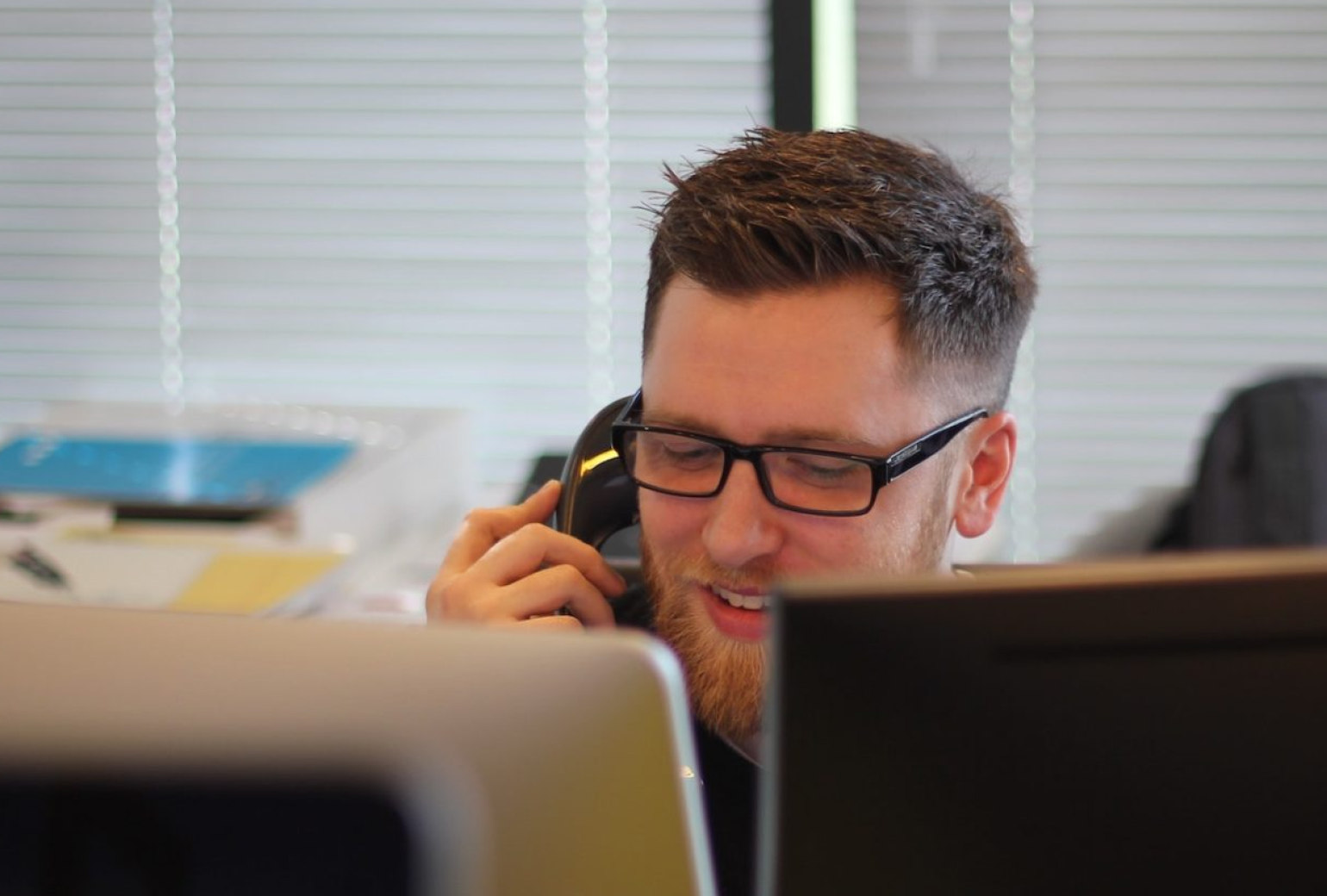 Man in glasses on the phone in front of two monitors