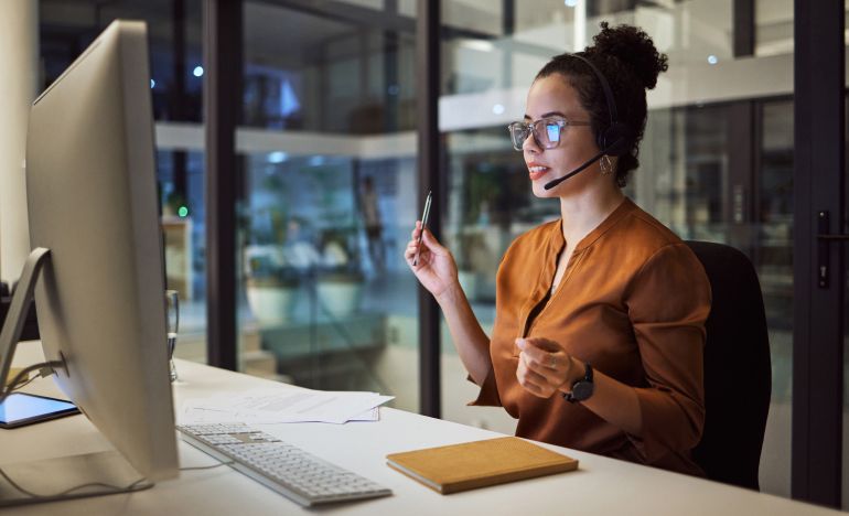 Woman in an orange shirt and phone headset in front of a computer monitor