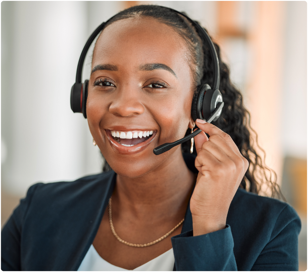 Smiling woman with a headset, wearing a blazer, in an office setting. She is engaging and friendly, conveying a professional tone.