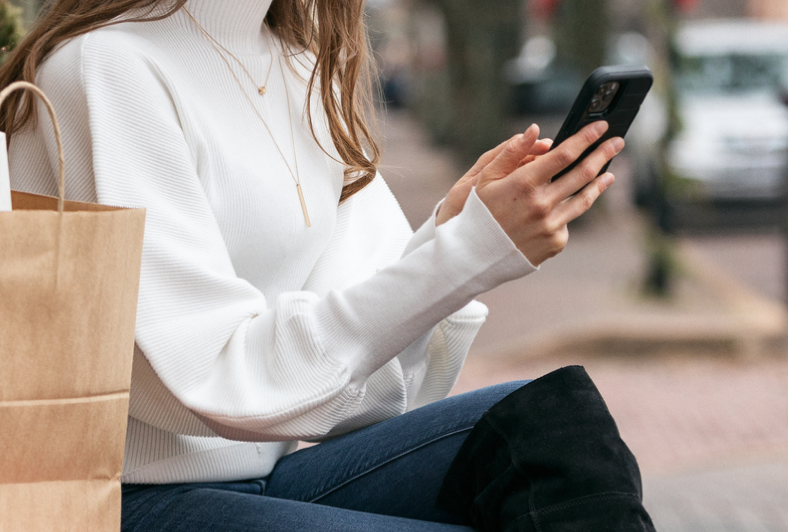 Seated woman holding a cellphone next to a shopping bag