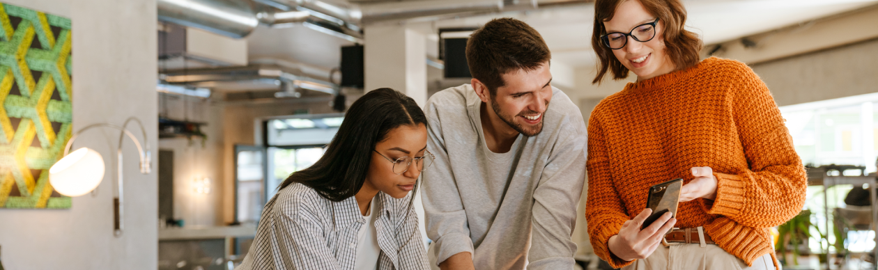 Three coworkers looking at one smartphone in an office