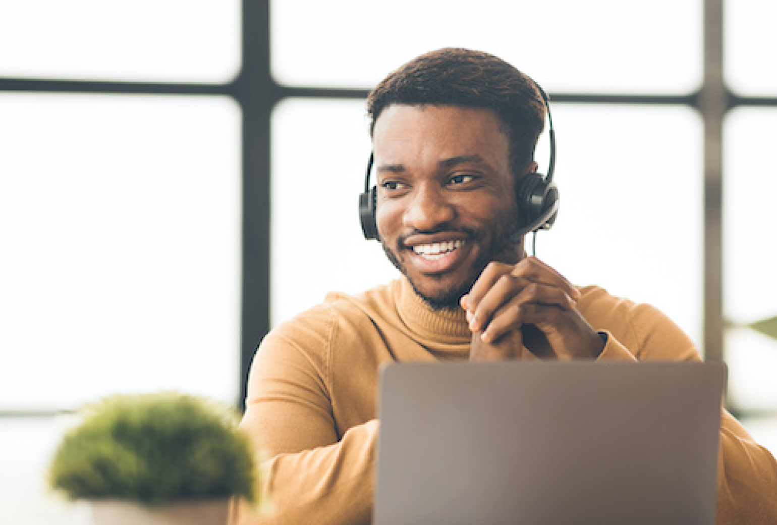 Man in an orange sweater smiling and wearing a phone headset