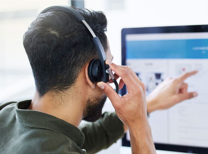 Man talking on a headset pointing to a computer screen