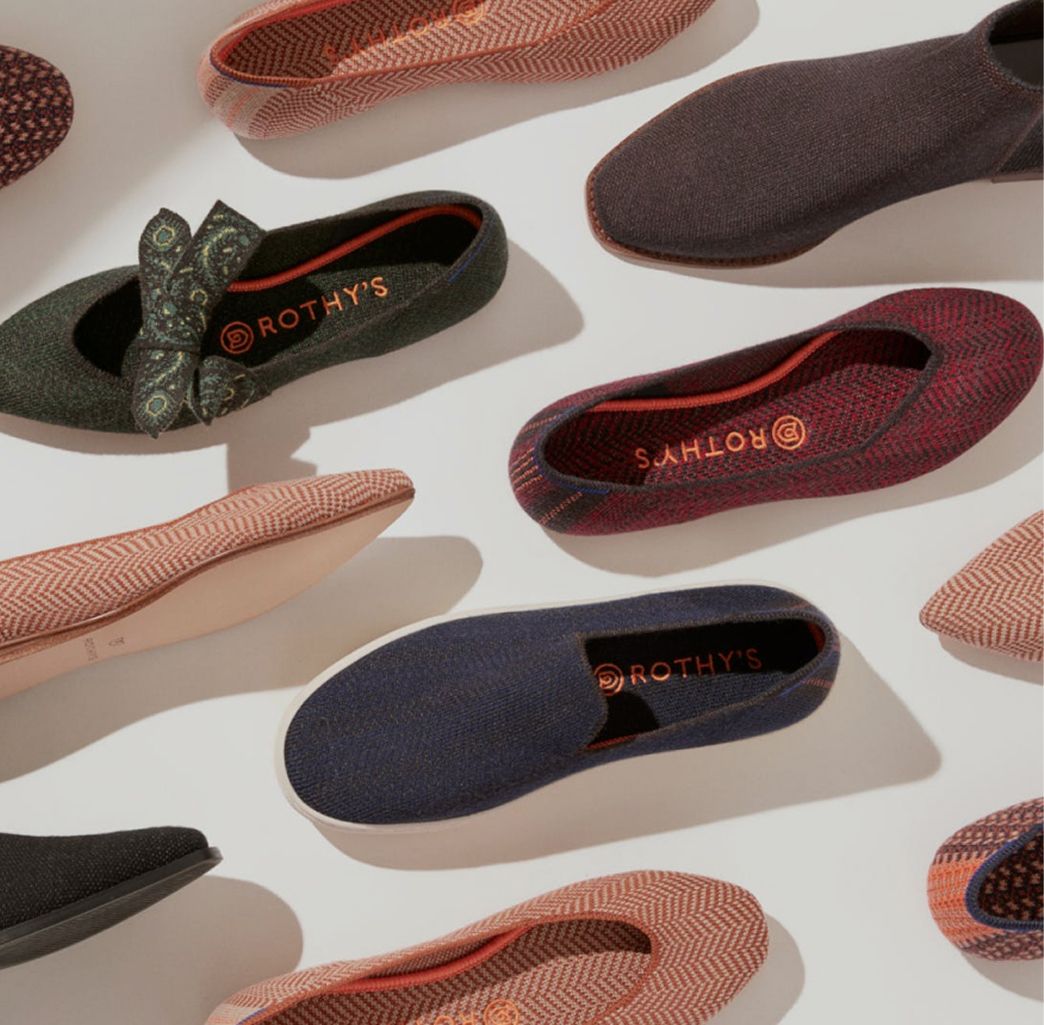 A collection of colorful slip-on shoes arranged diagonally on a light background. Patterns include herringbone and paisley, evoking a stylish and modern feel.