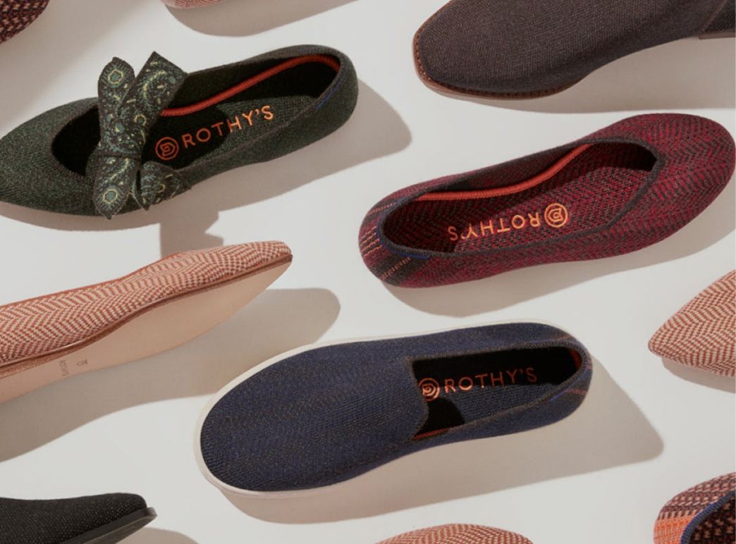 A collection of colorful slip-on shoes arranged diagonally on a light background. Patterns include herringbone and paisley, evoking a stylish and modern feel.