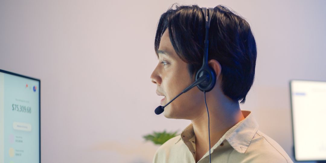 A person wearing a headset looks at a computer screen displaying financial data, including a colorful pie chart. The setting is professional and focused.