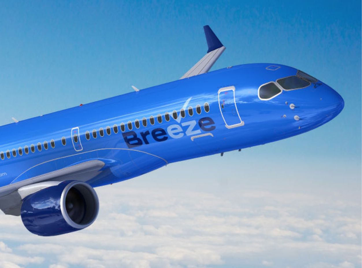 Blue airplane with "Breeze" logo flies above clouds against a clear blue sky, conveying a sense of modernity, speed, and freedom.