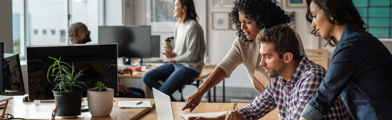 Three coworkers in an office discussing something on a laptop