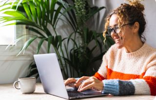Bespectacled woman smiling and typing on a laptop