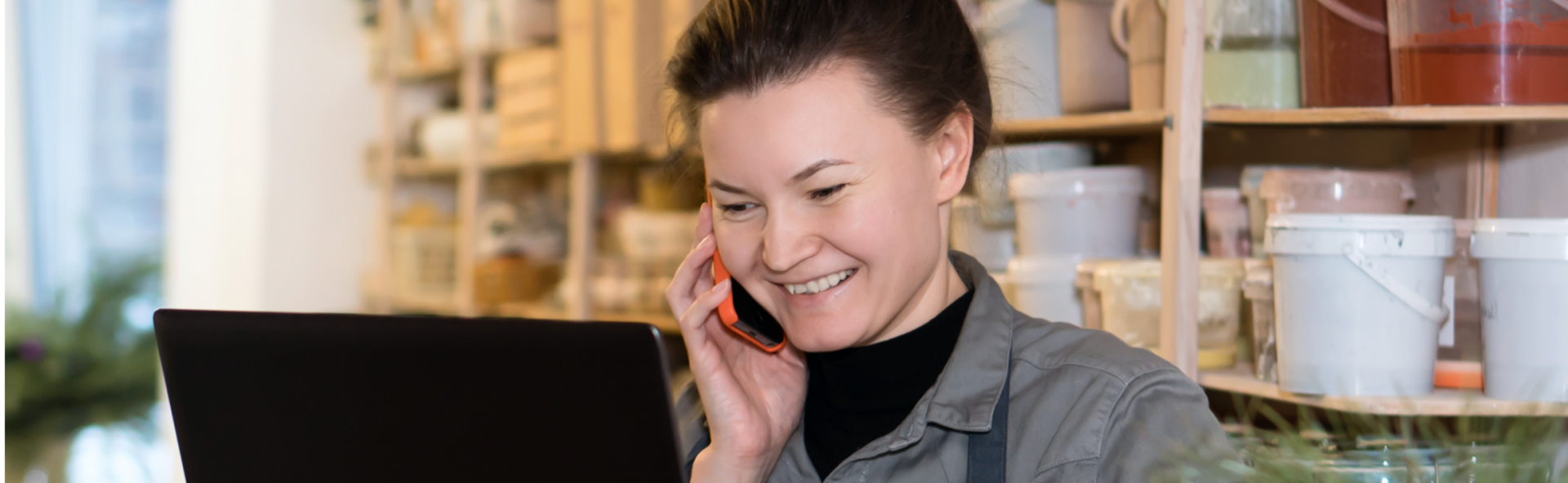 Smiling woman on a smartphone looking at a laptop