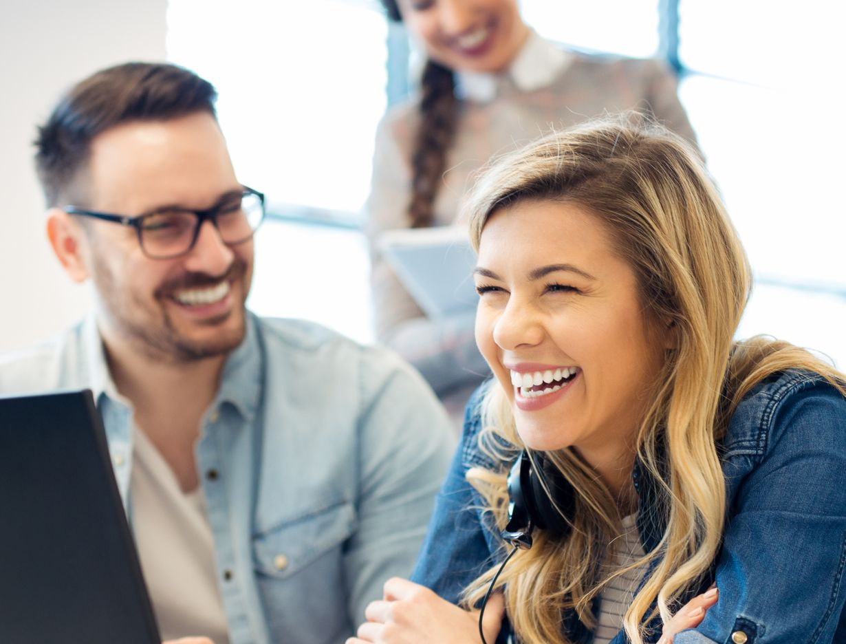 Three CX agents laughing while working side by side on laptops