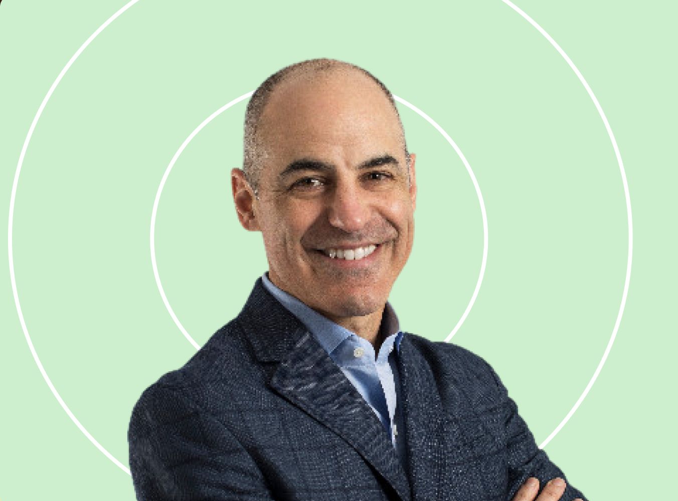 A man in a dark suit smiles confidently, standing with arms crossed against a light green background with subtle circular patterns.