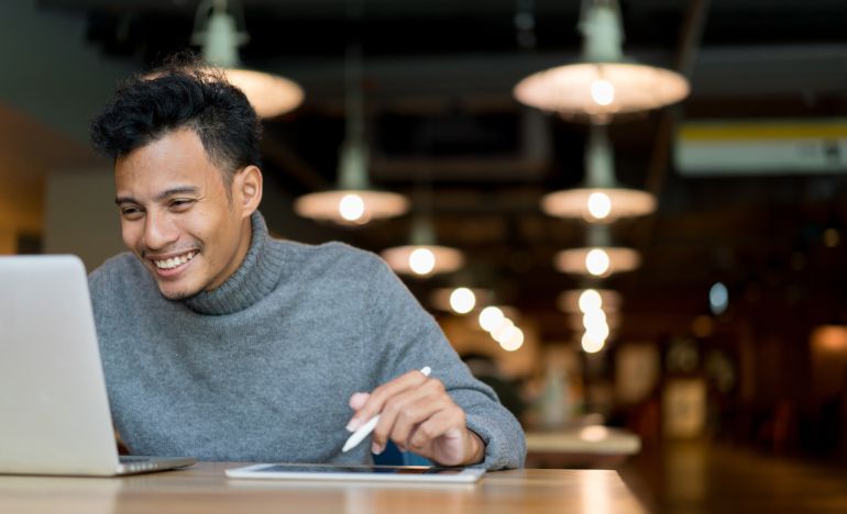 Man in a gray turtleneck smiling at a laptop
