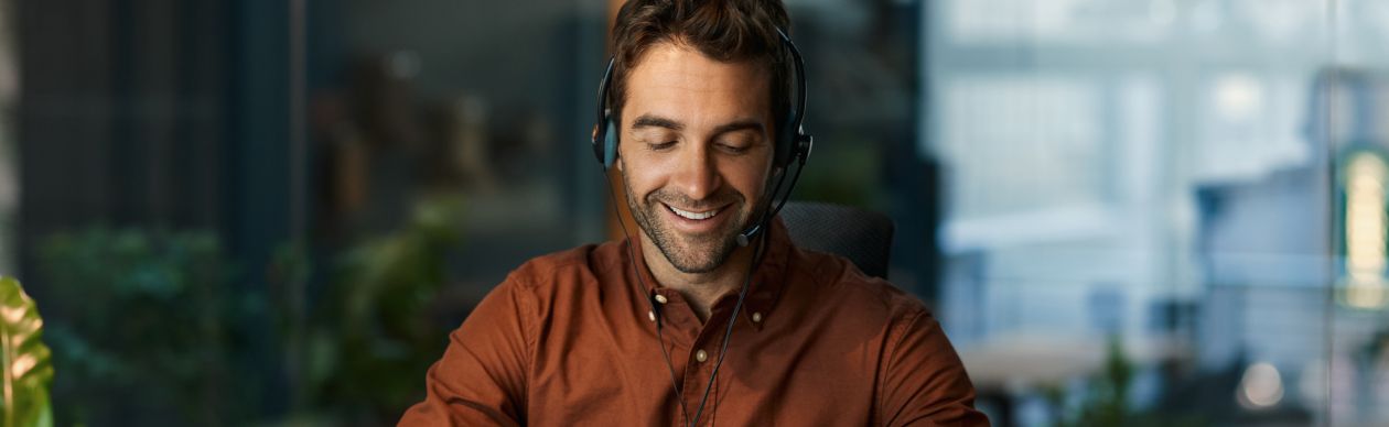 Man in a red shirt and phone headset smiling and looking at a laptop