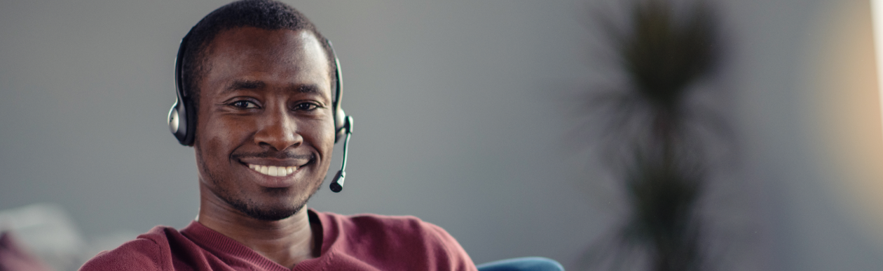 Smiling man in a red shirt with a phone headset working on a laptop
