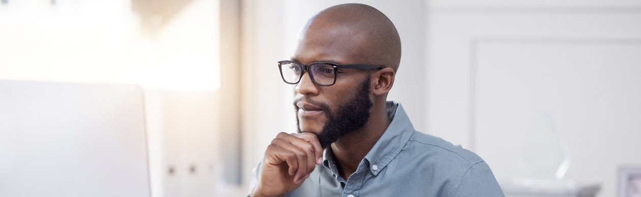 Bespectacled man looking ponderously at a laptop