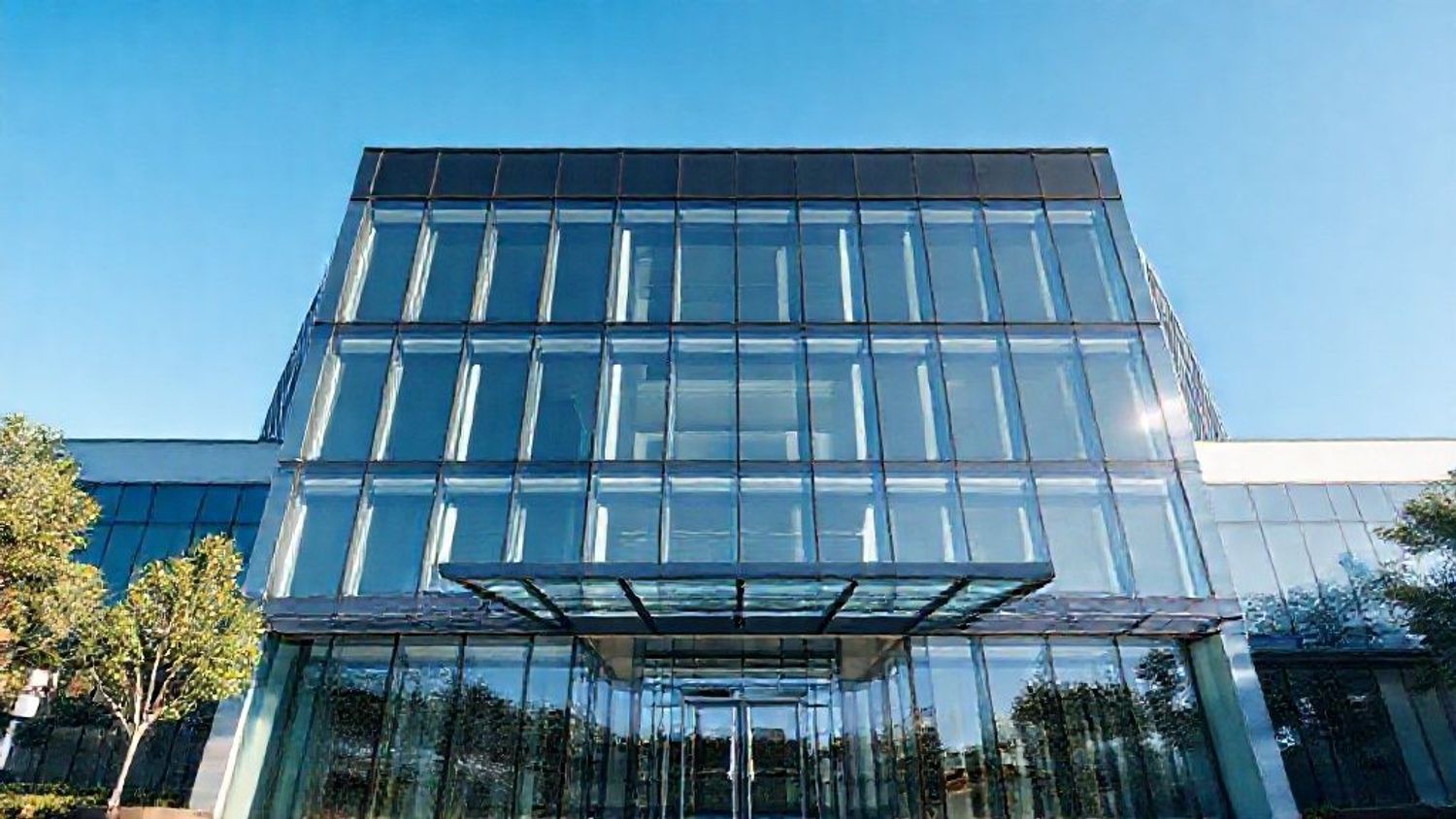 Modern office building with glass facade under blue sky.
