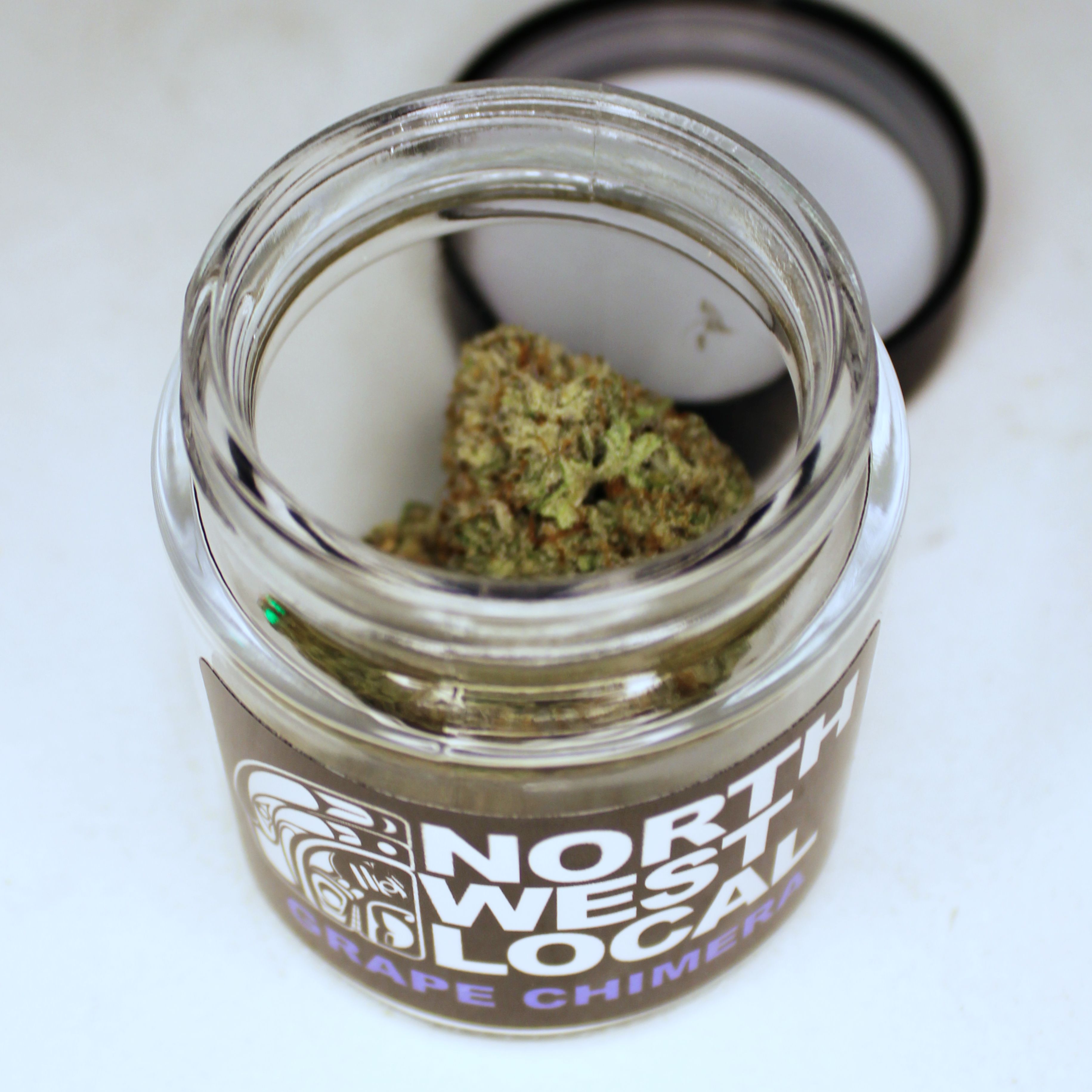 Northwest Local Grape Chimera eighth in a small glass jar with a black lid, the label showing the formline raven logo and the strain name in lavender lettering