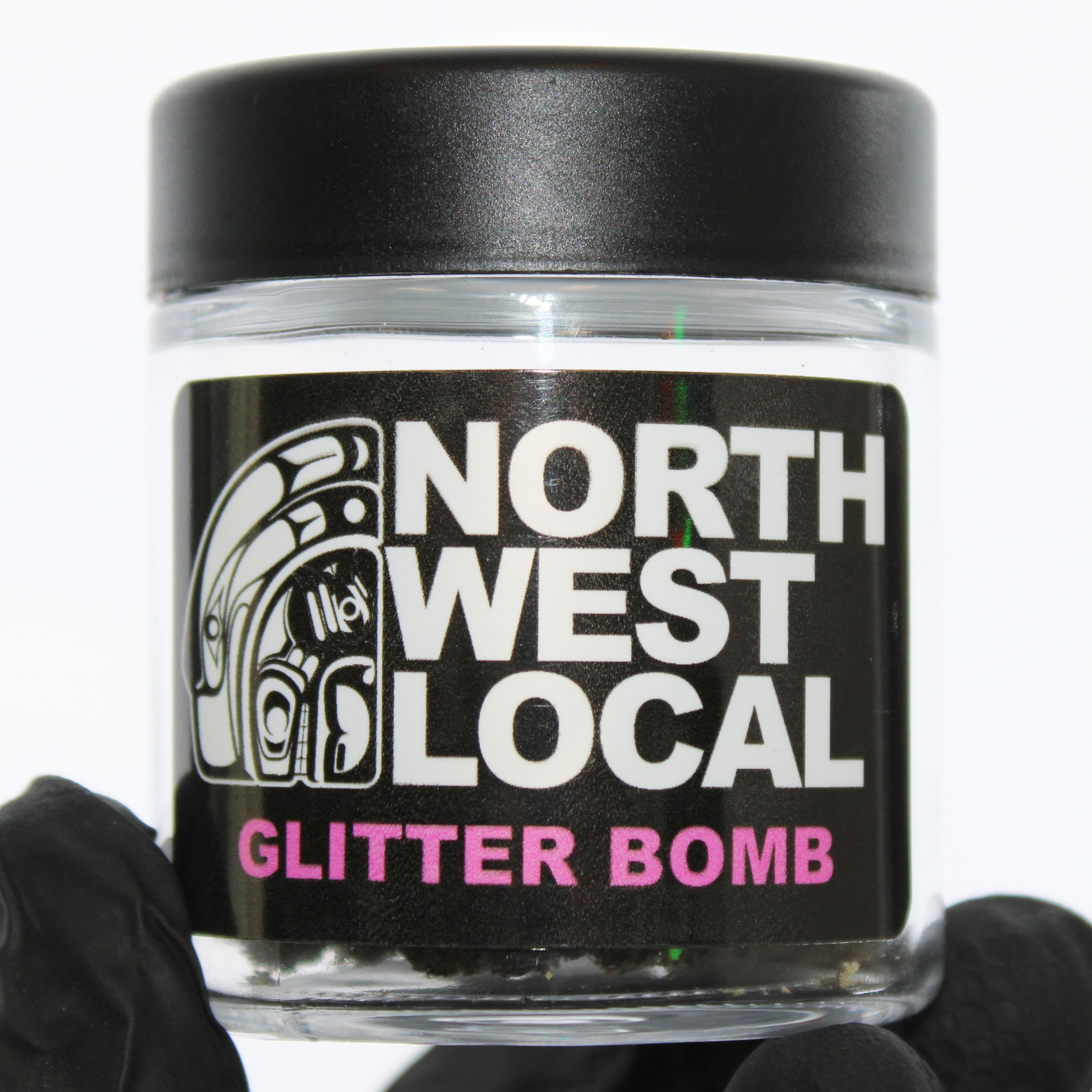 Northwest Local Glitter Bomb eighth in a small glass jar with a black lid, the label showing the formline raven logo and the strain name in pink lettering