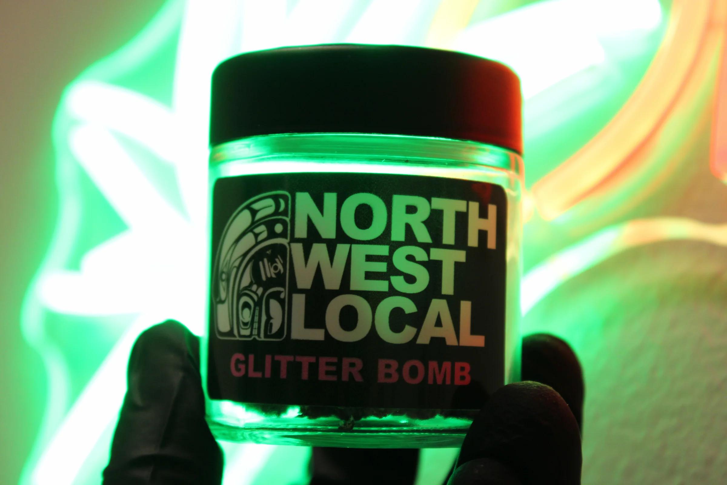 A Glitter Bomb jar held up to green and orange neon, the Northwest Local label lit from behind