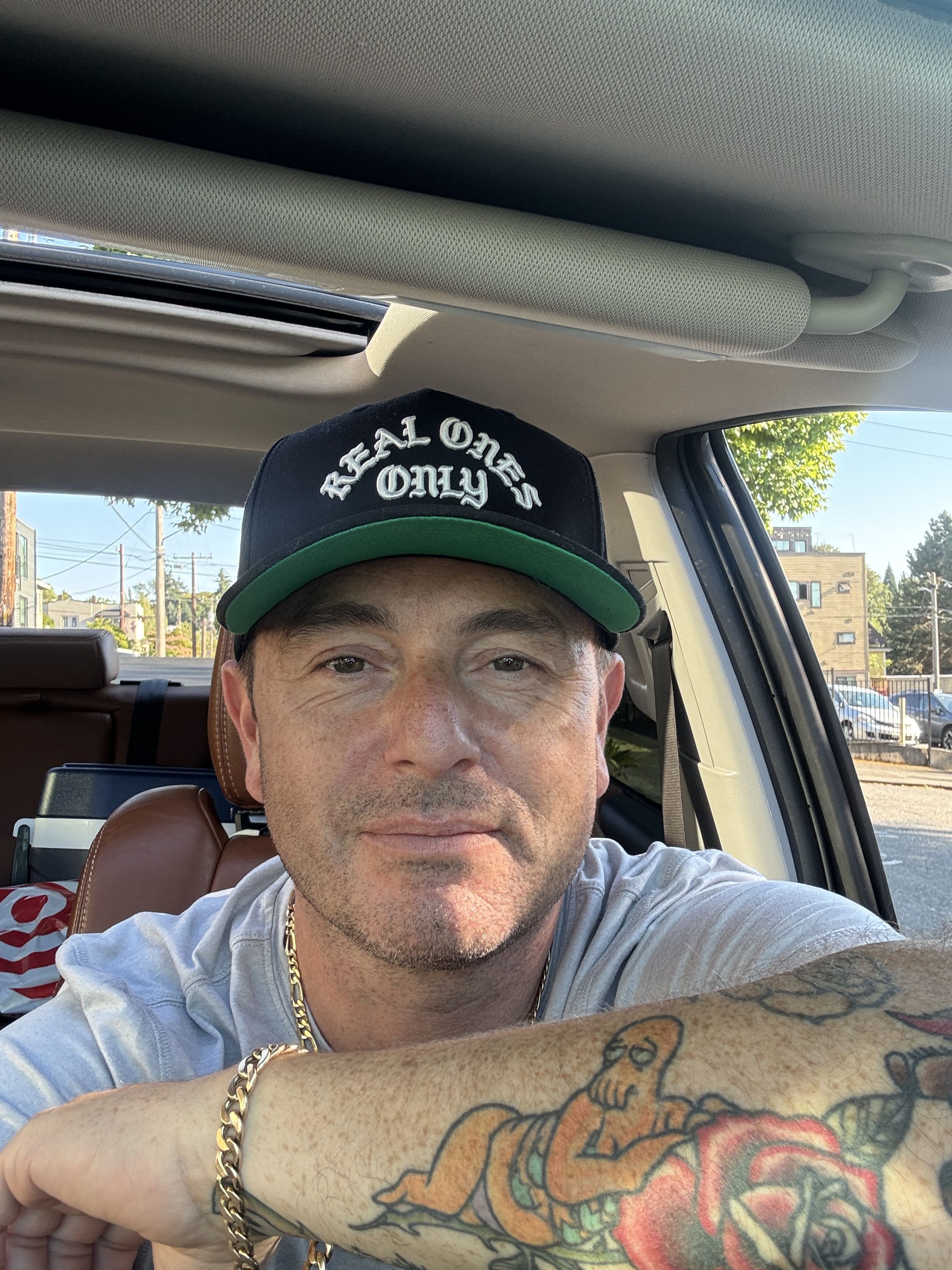 Ben Petty, co-founder of Northwest Local Cannabis, wearing a black Real Ones Only cap, seated in a car in Seattle.