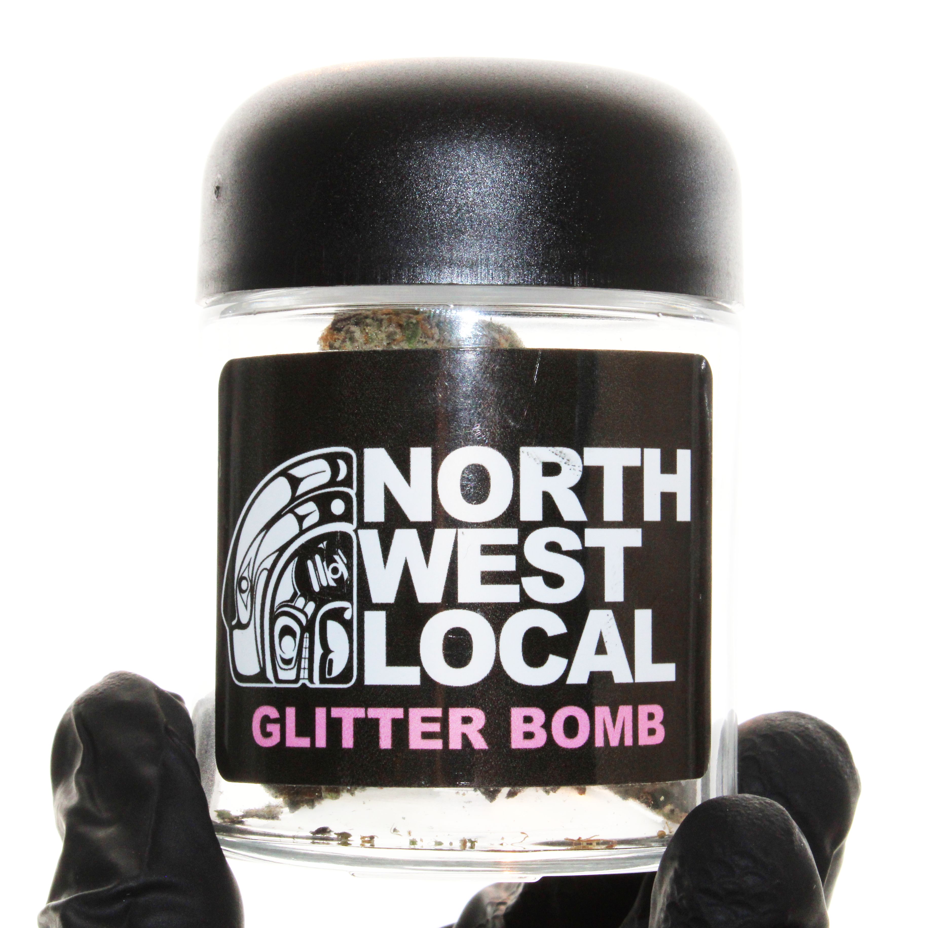 Gloved hands holding a Northwest Local Glitter Bomb quarter jar, with cured buds visible through the clear glass above the black label