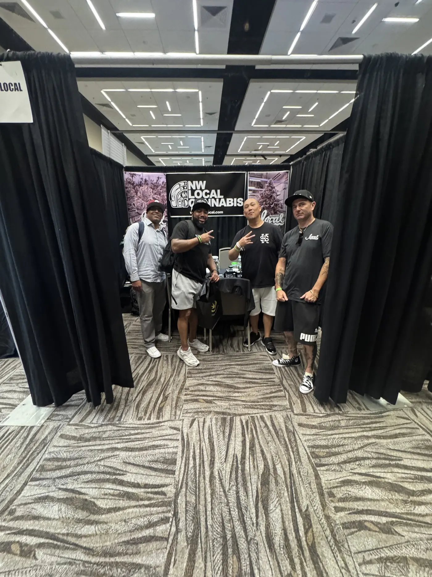 Four people at the entrance to the Northwest Local booth, several giving peace signs.