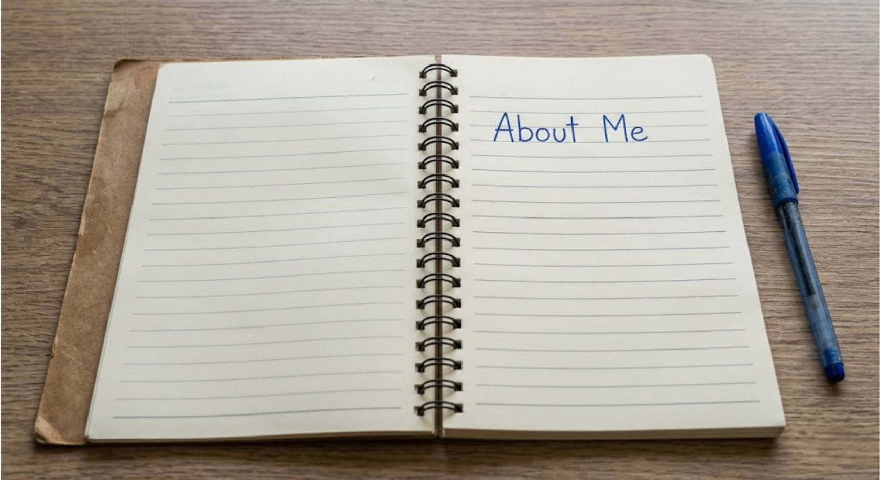 Un caiet cu spirală, deschis, cu cuvintele „About Me” scrise pe pagina din dreapta, lângă un pix albastru.