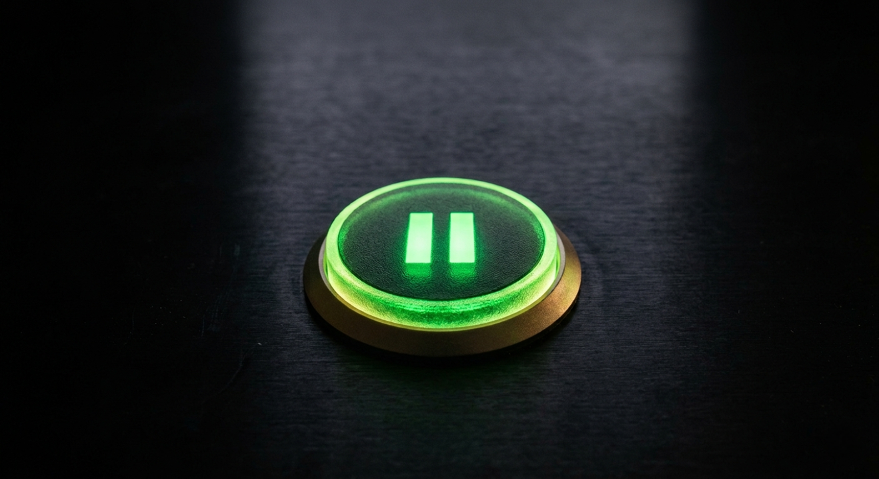 Un buton verde de pauză, aprins, pe o suprafață neagră.