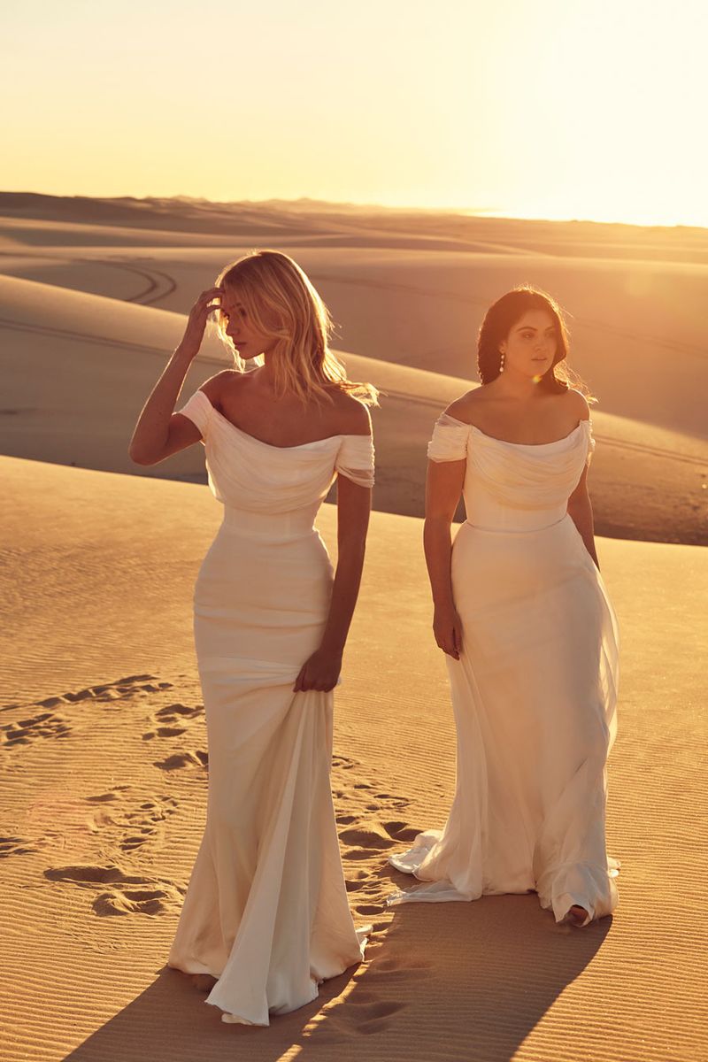 Two brides walking on the sand wearing Chosen Selene and Elane off the shoulder silk chiffon wedding dresses with draping across the bust.