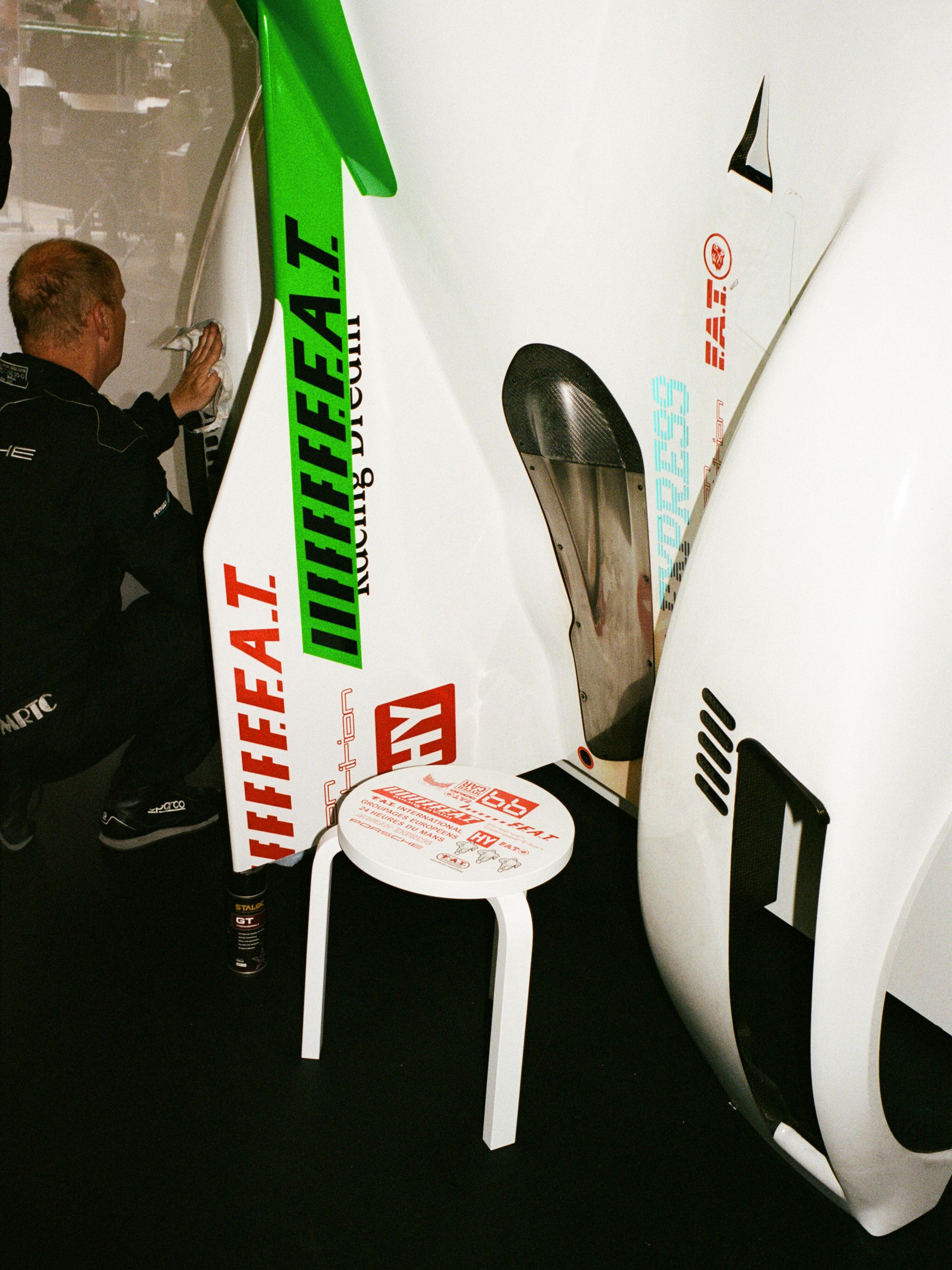 Proton Competition team member preparing the rear wing of the car for mounting, beside it sits the matching Le Mans collection Artek Stool 60 in white with red graphics